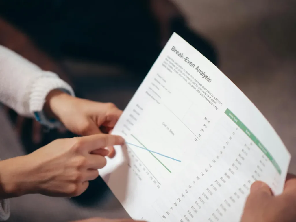 Tangan sedang menunjuk dokumen analisis break even point dalam rapat bisnis