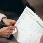 Tangan sedang menunjuk dokumen analisis break even point dalam rapat bisnis